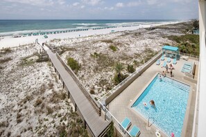 Une vue sur la plage avec une piscine, des parasols et des chaises longues.