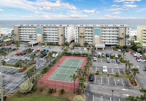 A hotel with multiple floors, a tennis court, and a parking lot with several cars.