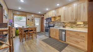 A modern kitchen with wooden cabinets, stainless steel appliances, and a dining area with wooden chairs. - Dock, Kayaks & Fire Pit: Solon Springs Lake Escape (Solon Springs)