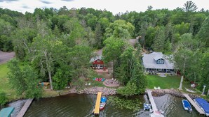 A lakeside property with docked boats, a cabin, and a large house with a porch. - Dock, Kayaks & Fire Pit: Solon Springs Lake Escape (Solon Springs)