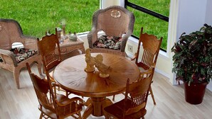 Un coin repas avec une table ronde en bois entourée de six chaises en bois, un canapé en osier et une plante en pot.