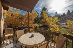 Un balcon avec une table ronde et des chaises, donnant sur un jardin aux couleurs automnales.