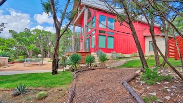 A red house with a garden path leading to it, surrounded by trees and plants.