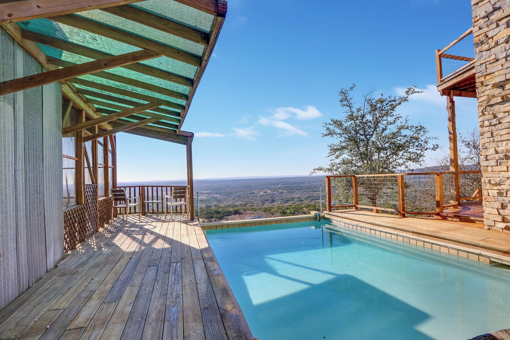 Eine Holzterrasse mit Pool, ein Steinhaus und Blick auf die Landschaft.