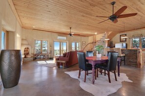 A spacious living area with a wooden ceiling, a dining table with chairs, a large vase, and a stone fireplace.