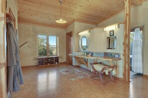 A room with a wooden ceiling, a large window, a mirror, a wooden bench, and a rug.
