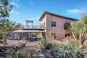 A modern two-story house with a covered patio, a hammock, and a stone facade.