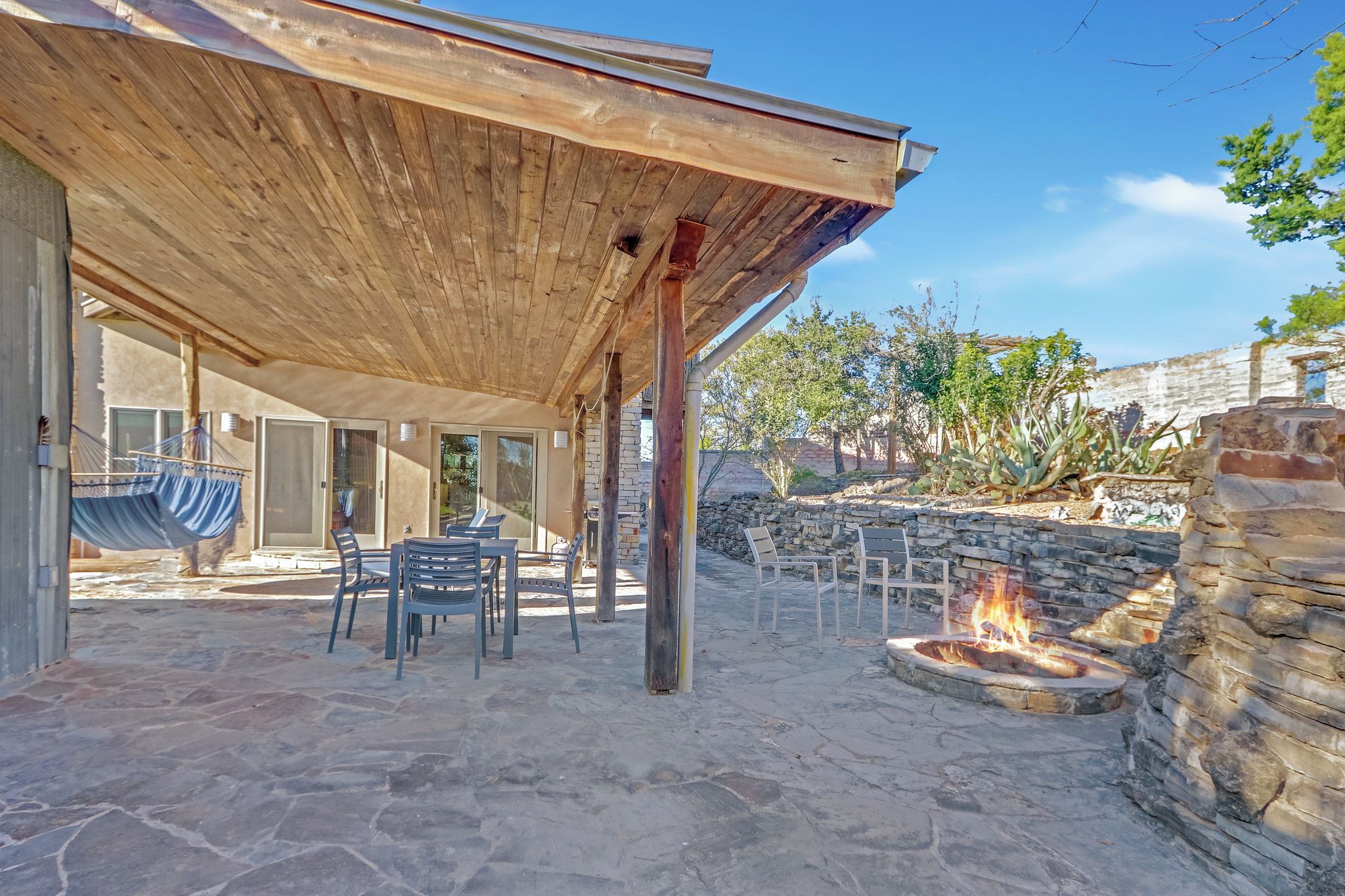 An outdoor patio with stone flooring, a wooden pergola, and a fire pit.