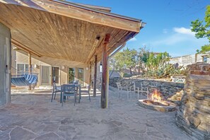 An outdoor patio with stone flooring, a wooden pergola, and a fire pit.
