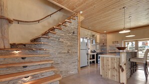 A modern kitchen with a stone wall, wooden staircase, and a bar area. - Casa Artista I Romantic, Pool, Hot tub, Endless Views (Wimberley)