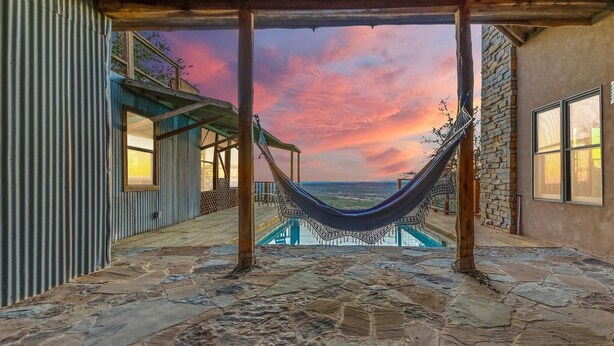 A hammock under a wooden pergola with a stone floor, overlooking a swimming pool and a scenic sunset view. - Casa Artista I Romantic, Pool, Hot tub, Endless Views (Wimberley)