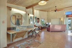A spacious living room with a wooden ceiling, a large mirror, a sofa, and a dining area with a table and chairs.