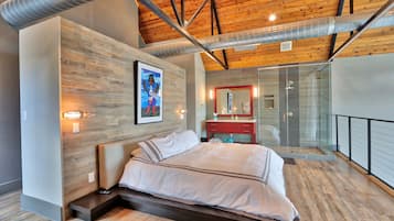 A modern bedroom with a wooden ceiling, a large bed, a glass shower, and a red vanity.