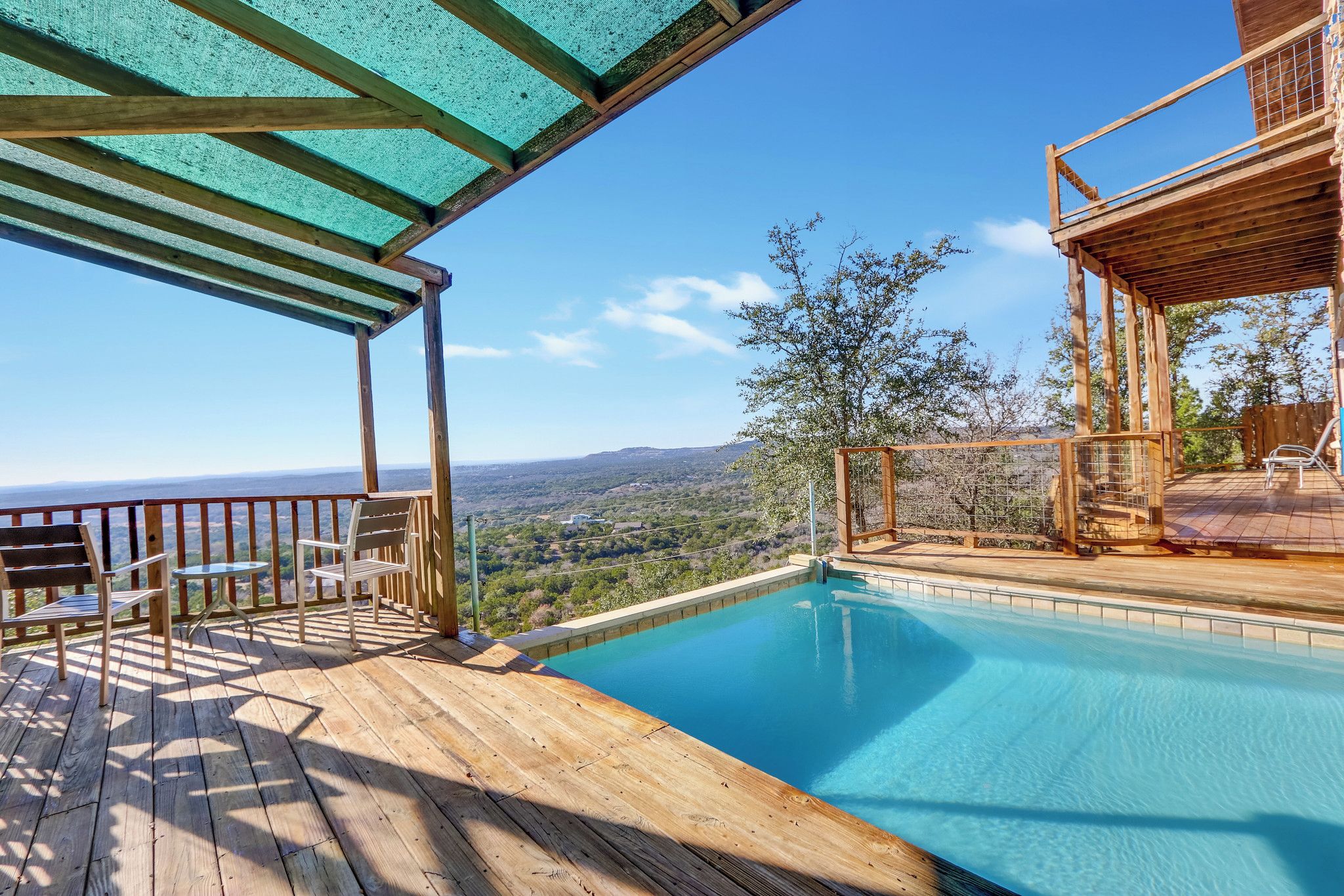 Una terraza de madera con piscina, mobiliario exterior y vistas al paisaje.