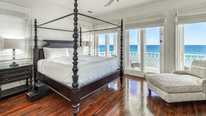 Una cama con dosel de madera, un ventilador de techo y vista al océano a través de amplios ventanales.