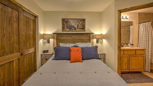 A bedroom with a bed, wooden wardrobe, bedside tables, a painting, and a bathroom visible through an open door.