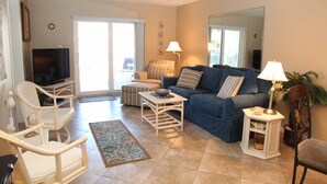 A living room with a sofa, chairs, a television, and a lamp. - Surfs up in this Cute 2bed/2ba condo! Ocean view! No drive Beach in NSB (New Smyrna Beach)