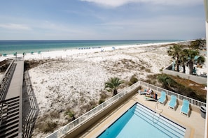 Vista da praia com área de piscina, espreguiçadeiras e uma praia de areia.