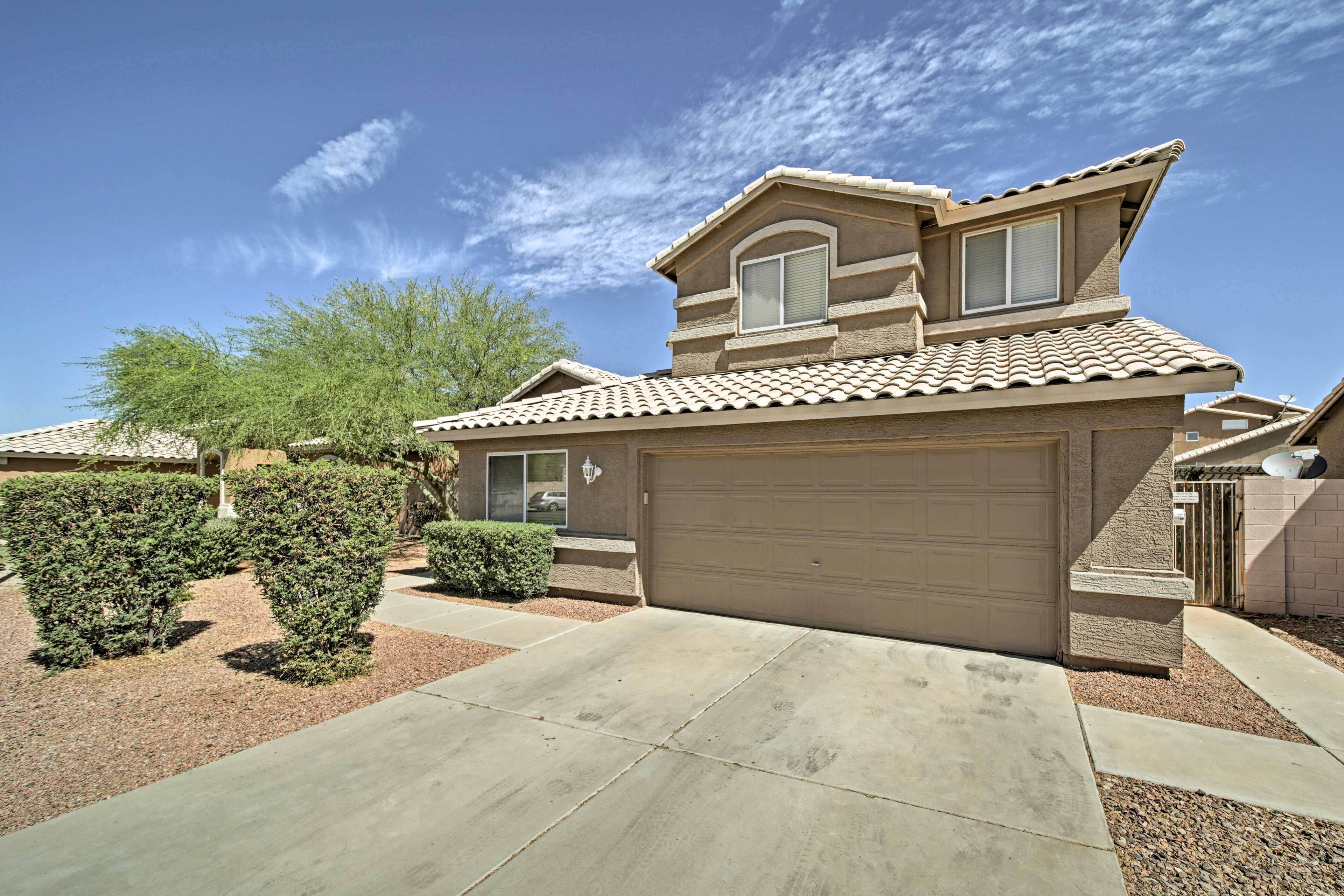 A residential house with a garage, a small front yard with trimmed bushes, and a clear blue sky.
