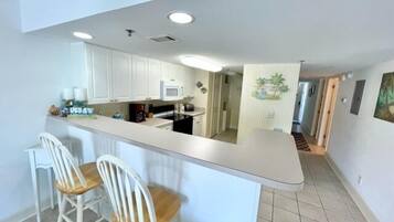 A kitchen with white cabinets, a white countertop, and two white bar stools.