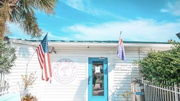 A white building with a blue door, two flags, and a logo reading "The Deck Beachfront Kitchen".