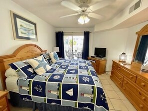 Quarto com cama, ventoinha no teto, televisão, penteadeira e janela com cortinas.
