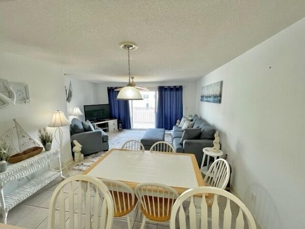 A modern living room with a dining area, a TV, and a balcony with blue curtains.