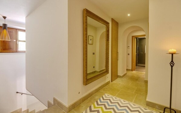 Un couloir avec un grand miroir, un tapis à motifs en zigzag et un lampadaire.