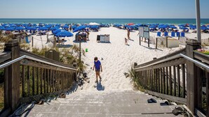 A beach with a wooden staircase leading down to the sand, surrounded by blue umbrellas and beach chairs. - WS B310: Resort Shores - The Perfect Gulf Retreat! (Fort Walton Beach)