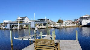 A wooden dock with a bench, a boat, and houses in the background.