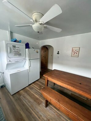 A compact kitchen with a white refrigerator, a built-in oven, a ceiling fan, and a wooden bench.