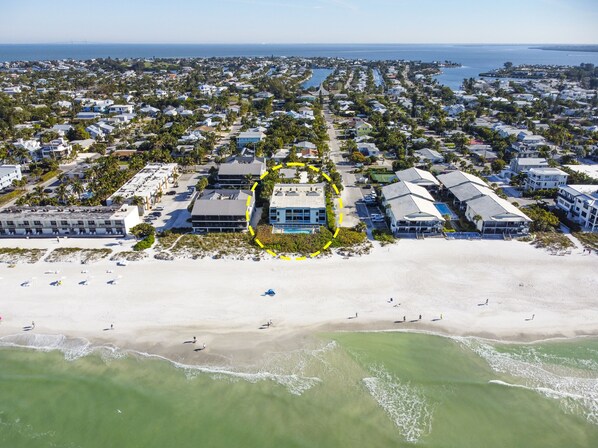 Vue aérienne d’un quartier résidentiel situé sur la côte, avec une plage, des maisons et une démarcation claire des limites des propriétés.