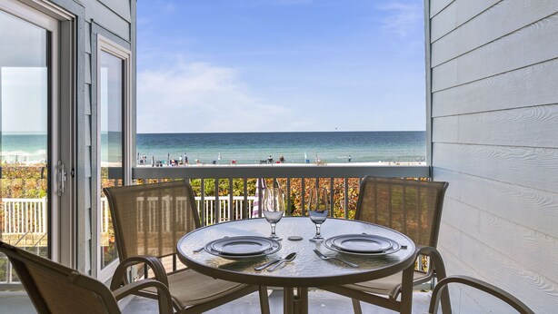 A balcony with a table set for two, overlooking a beach with people in the distance.