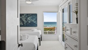 A hotel room with two beds, a world map on the wall, a balcony with a view of the ocean, and a ceiling fan.