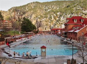 Una gran piscina al aire libre con múltiples carriles, rodeada de edificios y un paisaje montañoso.