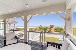 Un espacio al aire libre techado con vista al mar, muelle de madera y mobiliario exterior.