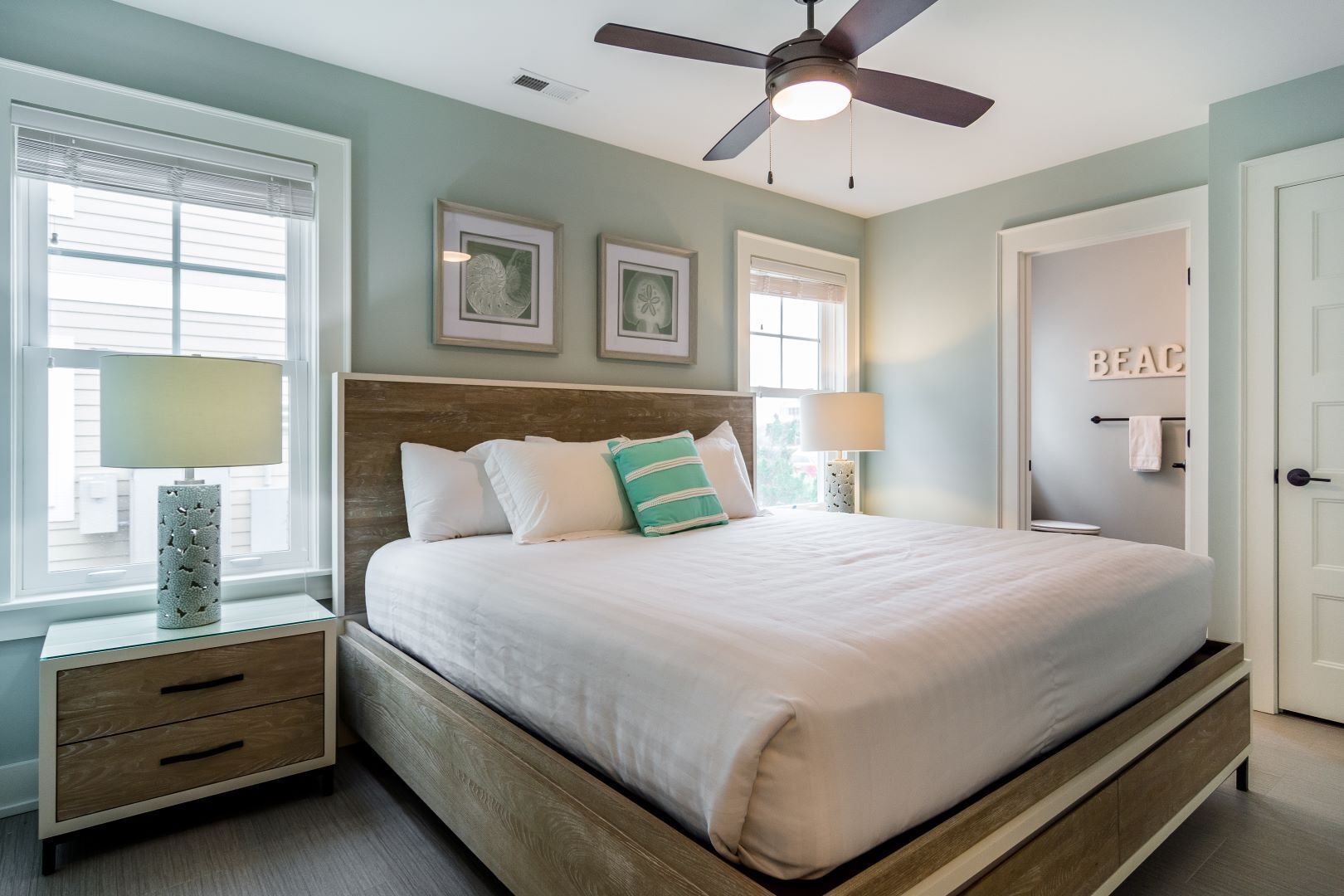 A bedroom with a bed, nightstands, a ceiling fan, and framed artwork on the wall.