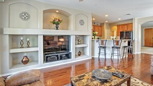 A spacious living room with a fireplace, a TV, and a dining area with bar stools. - Golf Course View! Group Getaway in Queen Creek (Queen Creek)