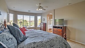 A bedroom with a bed, dresser, TV, and large windows. - Golf Course View! Group Getaway in Queen Creek (Queen Creek)