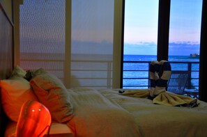 A bedroom with a bed, pillows, and a view of the sea through large windows.