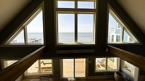 Een kamer met uitzicht op zee, een houten tafel en een bankje buiten.