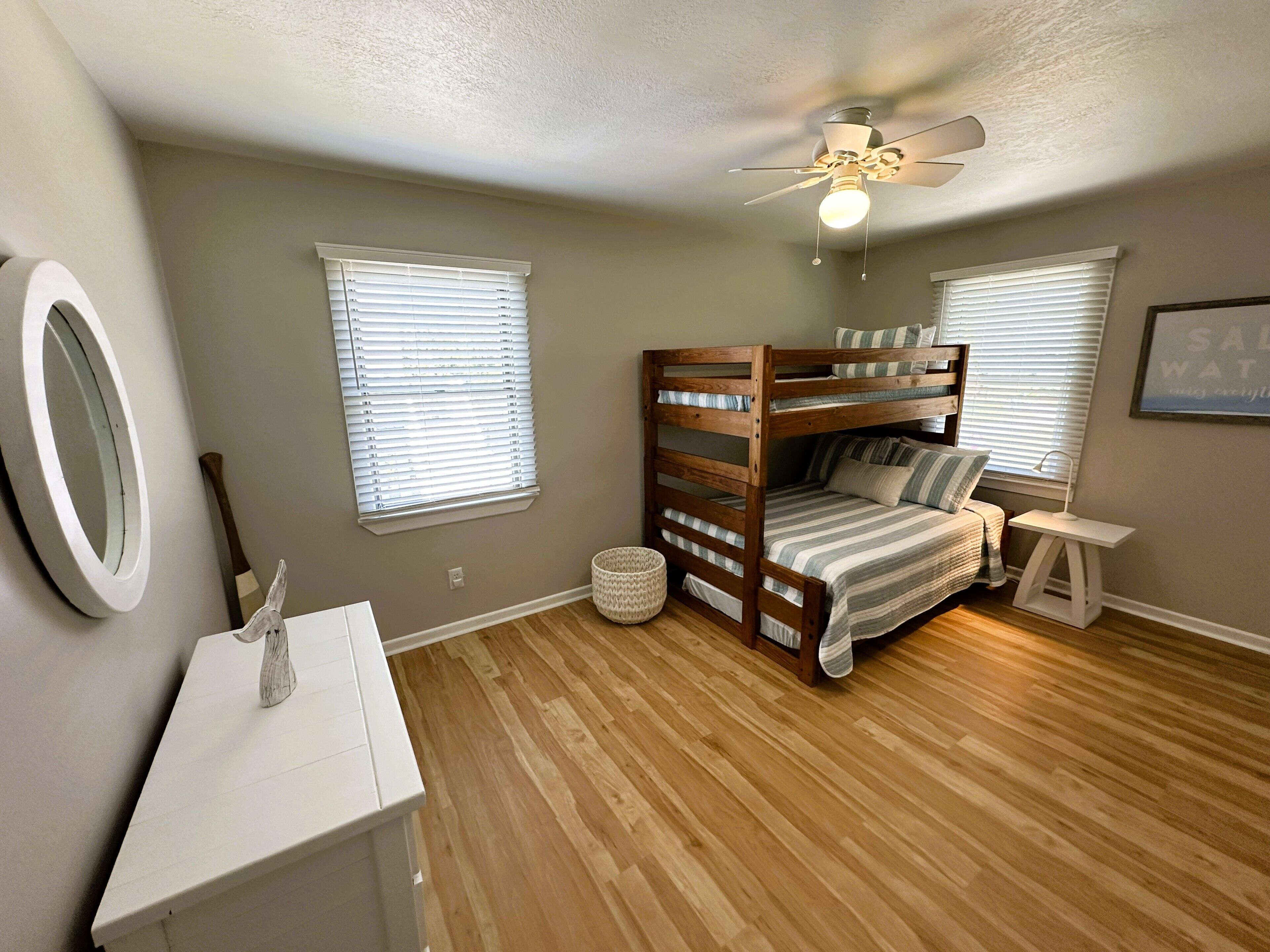 Une chambre d’enfant avec des lits superposés, un ventilateur de plafond et une petite table.