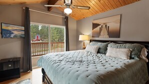 A bedroom with a large bed, a ceiling fan, a window with a view of a red barn, and a painting on the wall. - Five Pines - Beautifully updated gambrel cabin with Hot Tub and Fenced Yard! (Big Bear Lake)