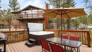 A wooden deck with a hot tub, barbecue grill, and outdoor seating area with a table and chairs. - Five Pines - Beautifully updated gambrel cabin with Hot Tub and Fenced Yard! (Big Bear Lake)