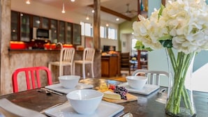 A dining area with a table set for two, a vase of flowers, and a kitchen in the background. - SoCo steps away + screened porch, artsy vibe (Austin)