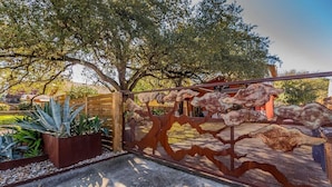 A metal gate with a unique design, leading to a paved area with plants and a tree. - SoCo steps away + screened porch, artsy vibe (Austin)