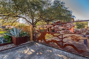 A metal gate with a unique design, leading to a paved area with plants and a wooden structure. - SoCo steps away + screened porch, artsy vibe (Austin)