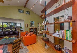 A spacious living area with a wooden floor, a sofa, a dining table, and a bookshelf filled with books and decorative items.
