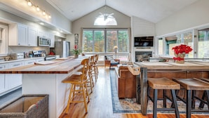 A spacious kitchen with a large island, wooden bar stools, and a view of autumn trees through large windows. - White Mountains Home w/ Hot Tub - Walk to Town! (North Conway)