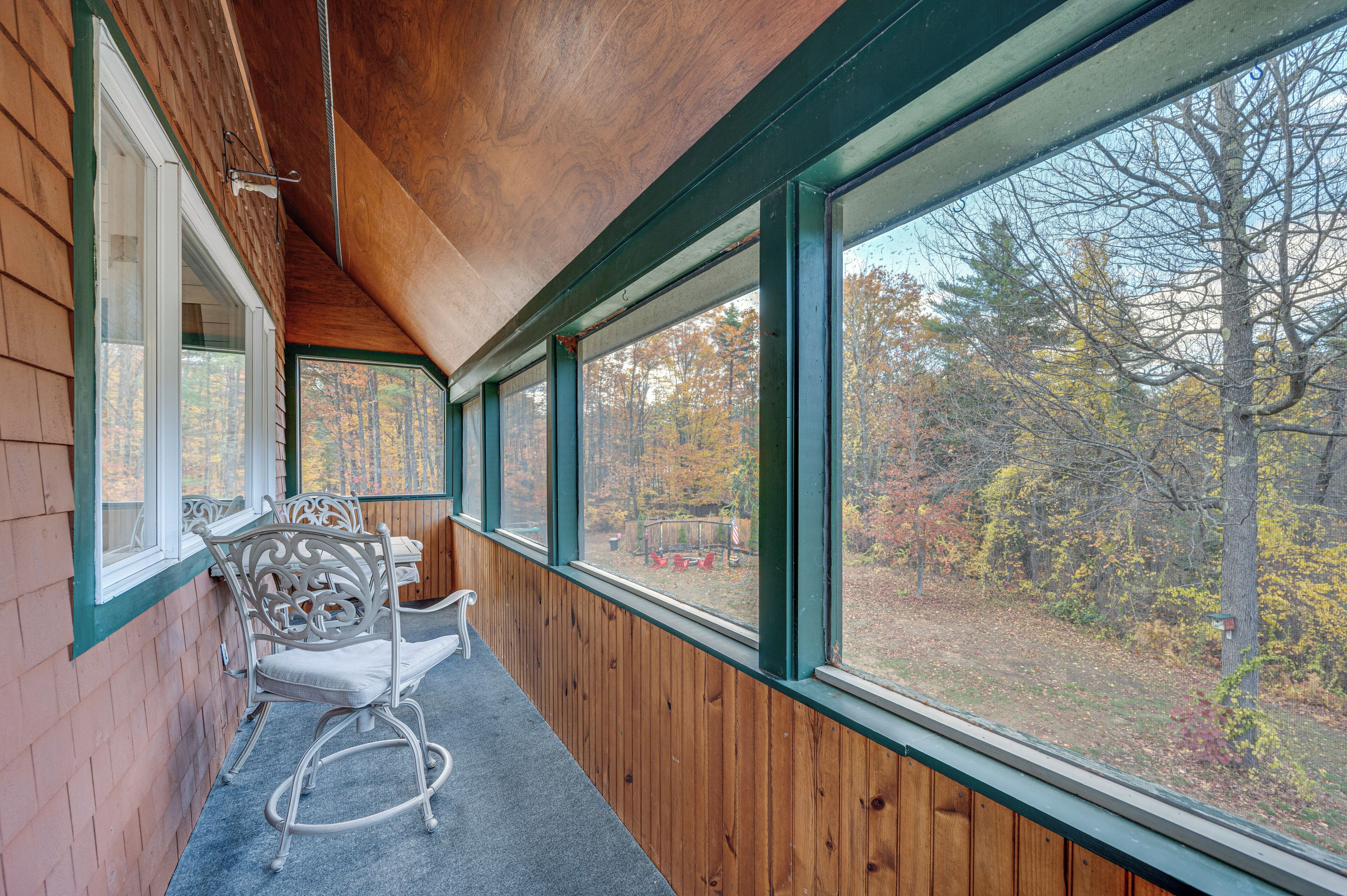A wooden interior with large windows, a chair, and a view of autumn trees.
